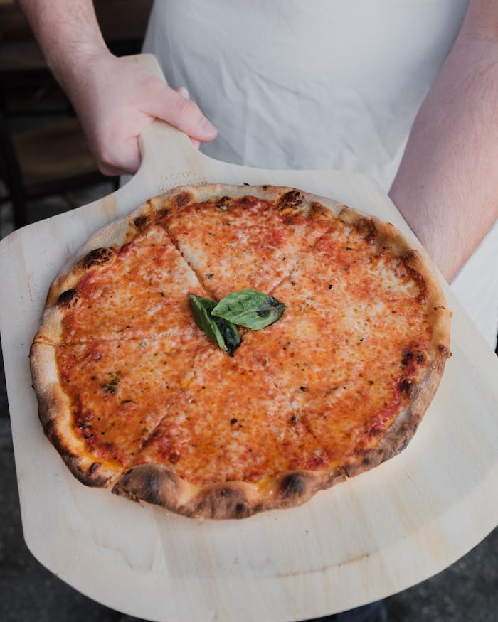 pexels-photo-9424919 Freshly baked cheese pizza with basil on wooden paddle, ready to serve.